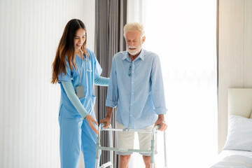 Care worker helping elderly man get out of bed and walk around the room.