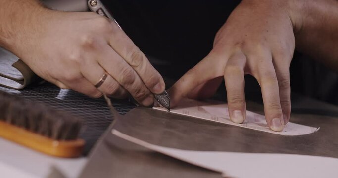 Close up view of tailor hands with knife passing around pattern on leather piece preparing blanks for making shoes, slow motion 4k