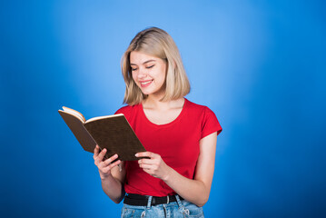 Young and attractive caucasian blonde girl in casual clothes smiling, holding and reading a book...