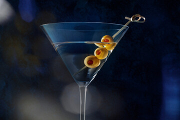 Martini, a glass with spicy olives, on a dark background. Alcoholic drink with bokeh, toned image,...