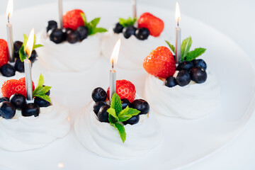 Meringue dessert Pavlova cake nests with fresh strawberries and blueberries with mint on the white plate with burning candles. Happy Birthday cake idea. Close up. Selective focus