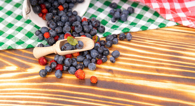 Blueberries and strawberries on a wooden spoon on a wooden table with copy space. forest goda