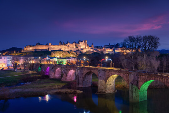 Medieval city of Carcassonne Pont Vieux bridge lit up at night during Christmas with pink clouds from the sunset