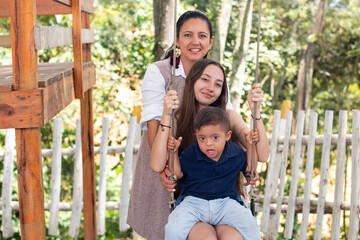 Child with downs syndrome rides swing with his mother and sister.