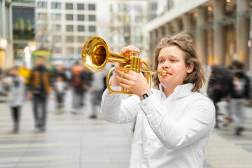 Young caucasian long-haired blond man in white shirt playing jazz on golden trumpet with pleasure...