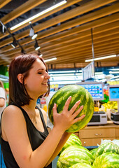 young woman in supermarket choosing watermelon