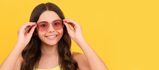happy child in summer glasses has curly hair on yellow background, beach fashion. Child face, horizontal poster, teenager girl isolated portrait, banner with copy space.