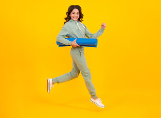 Sportswear advertising concept. Run and jump. Teenager child girl in tracksuits jogging suit posing in the studio hold fitness mat.
