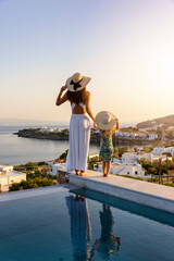 A beautiful woman and her daughter are standing by the pool and enjoying the summer sunset over the Aegean sea, Greece