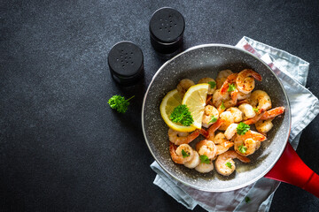 Frying shrimps with lemon in the frying pan. Top view image on black.