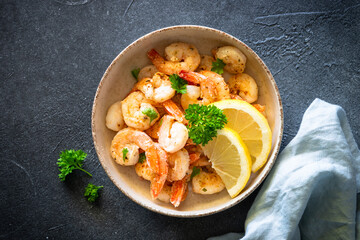 Frying shrimps with lemon and herbs in the craft bawl. Top view image on black.
