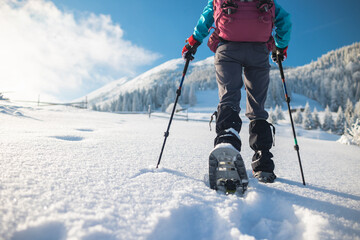 A woman with a backpack in snowshoes climbs a snowy mountain