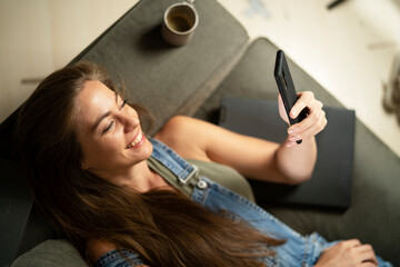 Happy young woman using the phone at home. Excited woman enjoying in the living room..