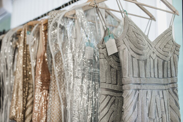 Beautiful dresses with embroidery, beads and sequins hang on hangers in a luxury clothing store.