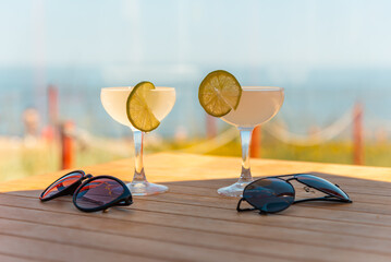 Fototapeta na wymiar Two drinking glasses of Margarita cocktails. Beach bar concept. Summer alcoholic cocktails,sunglasses on table bar, sea on background.