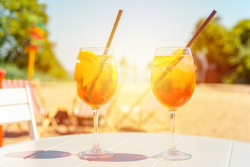 Two glasses of orange spritz aperol drink cocktail on table outdoors sunset with sea and trees view blurred background.