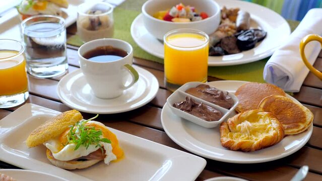 Delicious breakfast in hotel. Table with various food, eggs Benedict, fresh pastry, juices, tea and coffee drinks. Morning food in tropical resort. Dinner in outdoor cafe. 