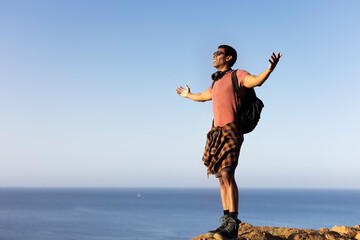 Obraz premium Young man standing on the stone with raised up arms. Tourist man on the top of the mountain.