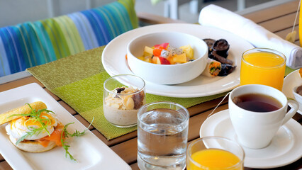 Hotel table with breakfast food. Served meal in modern tropical resort. Dinner for two in restaurant with fresh fruits, juices, eggs and cereals. Holiday, vacation, weekend concept