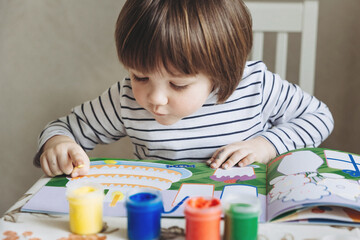 Finger painting. Portrait of cute little boy painting with fingers at home. Close-up of child's hand in colorful paints. Early education concept. Sensory play. Development of fine motor skills.