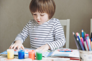 Finger painting. Portrait of cute little boy painting with fingers at home. Close-up of child's hand in colorful paints. Early education concept. Sensory play. Development of fine motor skills.