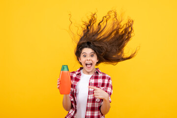 Amazed teenager. Teenager child girl showing bottle shampoo conditioners or shower gel. Hair cosmetic product. Bottle for advertising mock up copy space. Excited teen girl.