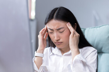 Close-up photo of business woman tired in office, Asian female worker holding hands on head, having...
