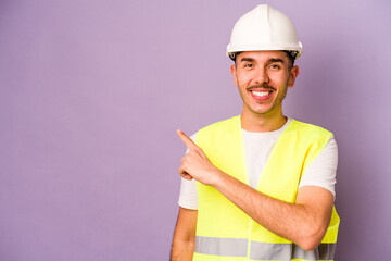 Young hispanic worker man isolated on purple background smiling and pointing aside, showing...