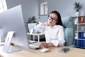Overtired Asian woman office worker, has severe neck pain, massages neck muscles with hand, female...