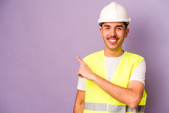Young hispanic worker man isolated on purple background smiling and pointing aside, showing something at blank space.