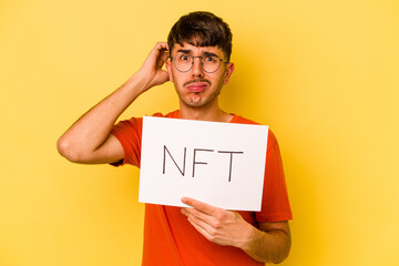 Young hispanic man holding nft placard isolated on yellow background being shocked, she has...