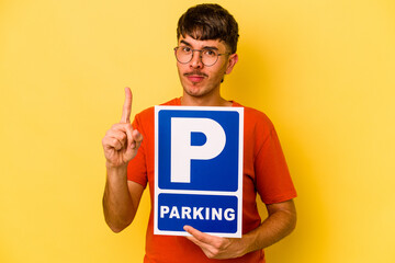 Young hispanic man holding parking placard isolated on yellow background showing number one with finger.