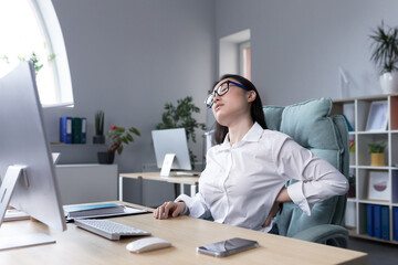Tired female office worker massaging her back, Asian business woman has severe back and lower back...
