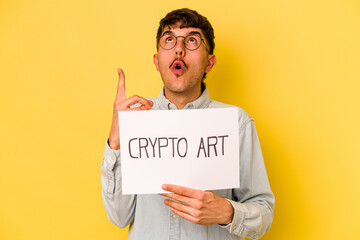 Young hispanic man holding crypto art placard isolated on yellow background pointing upside with opened mouth.