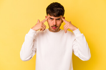 Young caucasian man isolated on yellow background focused on a task, keeping forefingers pointing head.