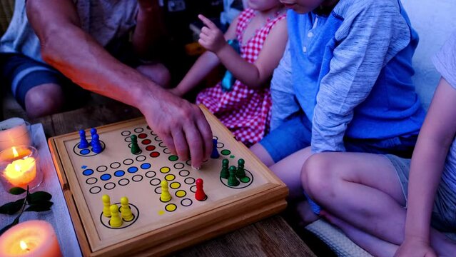 children and adults roll dice and move chips, wooden desktop with colorful figurines, concept of spending an evening together with whole family, learning rules of game, board games for whole family
