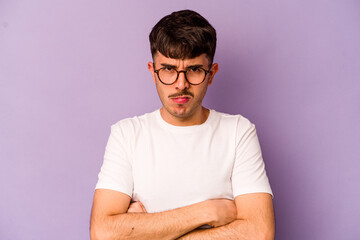 Young caucasian man isolated on purple background frowning face in displeasure, keeps arms folded.