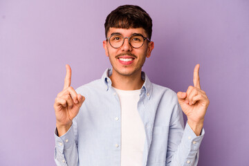 Young caucasian man isolated on purple background indicates with both fore fingers up showing a...