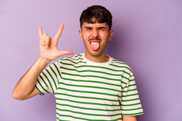 Young caucasian man isolated on purple background showing rock gesture with fingers