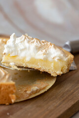 Lemon meringue sliced and being served with a cake slicer. On a wooden chopping board