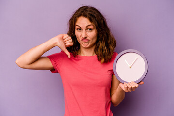 Young caucasian woman holding a clock isolated on yellow background showing a dislike gesture, thumbs down. Disagreement concept.