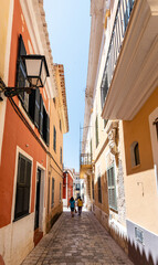 Fototapeta na wymiar Deux personnes marchent dans une ruelle à Ciutadella