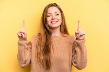 Young caucasian woman isolated on yellow background indicates with both fore fingers up showing a...