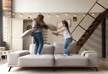 Two kids sisters girls playing with pillows at home, enjoying weekend spend time together.