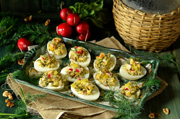 Stuffed eggs with dill and radish on a rustic platter on a dark background