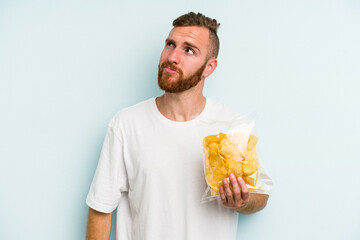 Young caucasian man holding crisps isolated on blue background dreaming of achieving goals and purposes