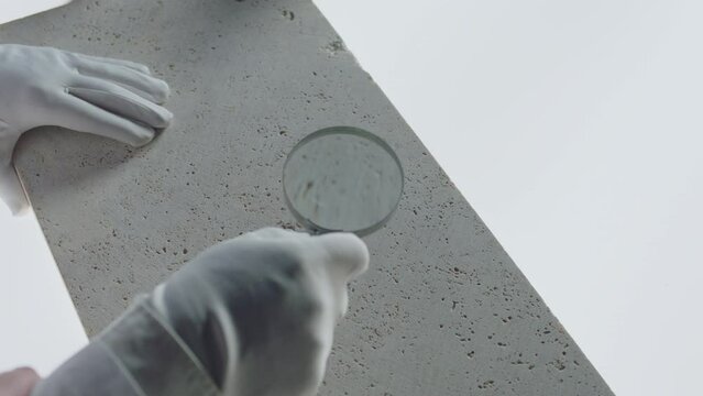Construction laboratory testing the quality density of natural travertine stone . Worker of laboratory explore stone by loupe . Close up view of hands with gloves . Shot on ARRI Alexa cinema camera