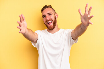 Young caucasian man isolated on yellow background feels confident giving a hug to the camera.