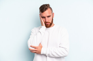 Young caucasian man isolated on blue background who is bored, fatigued and need a relax day.