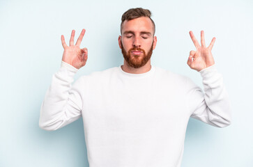 Young caucasian man isolated on blue background relaxes after hard working day, she is performing yoga.